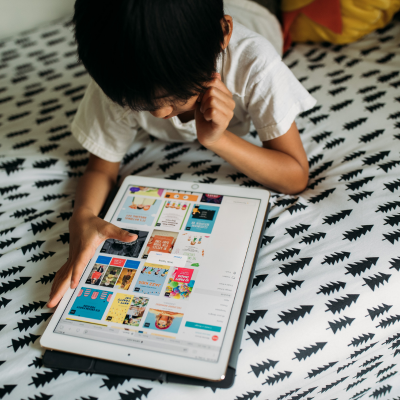 A child laying on a bed looking at tablet computer screen