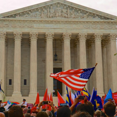 A photo of the Supreme Court of the United States with a protest in front, and flags waving.