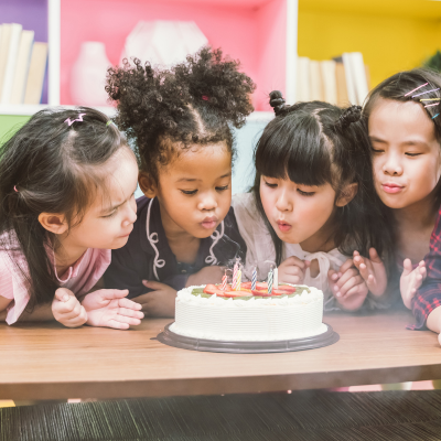 Child blowing out birthday candles with three friends