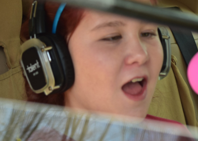 A child singing into a microphone while sitting in the back of her car. Child is wearing headphones and we see her from the front.