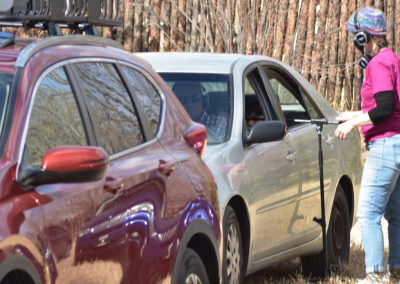 A woman standing next to a car in the field adjusting a microphone stand.