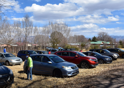 A lot of cars parked on an empty, dry field. One person is standing between two cars looking busy.