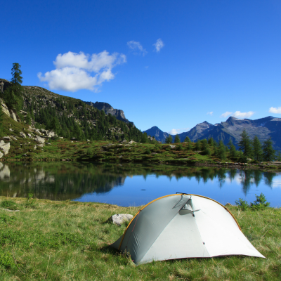 Camping With Kids - Camping by the lake A grey tent set up on a grassy area next to a pristine mountain lake with a deep azure sky.<br />