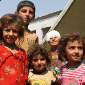Five children in a refugee camp. One in back has bandaged eyes. Kids are smiling but it's clear life is difficult.