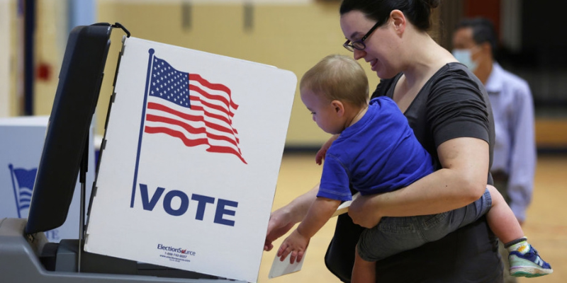 A woman at a voting booth holding a toddler 